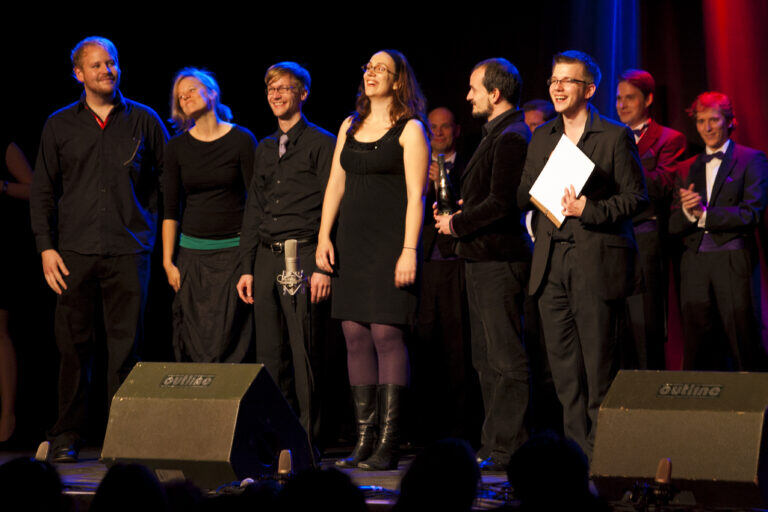 Preisträgerfoto auf der Bühne mit zwei Sängerinnen und vier Sängern